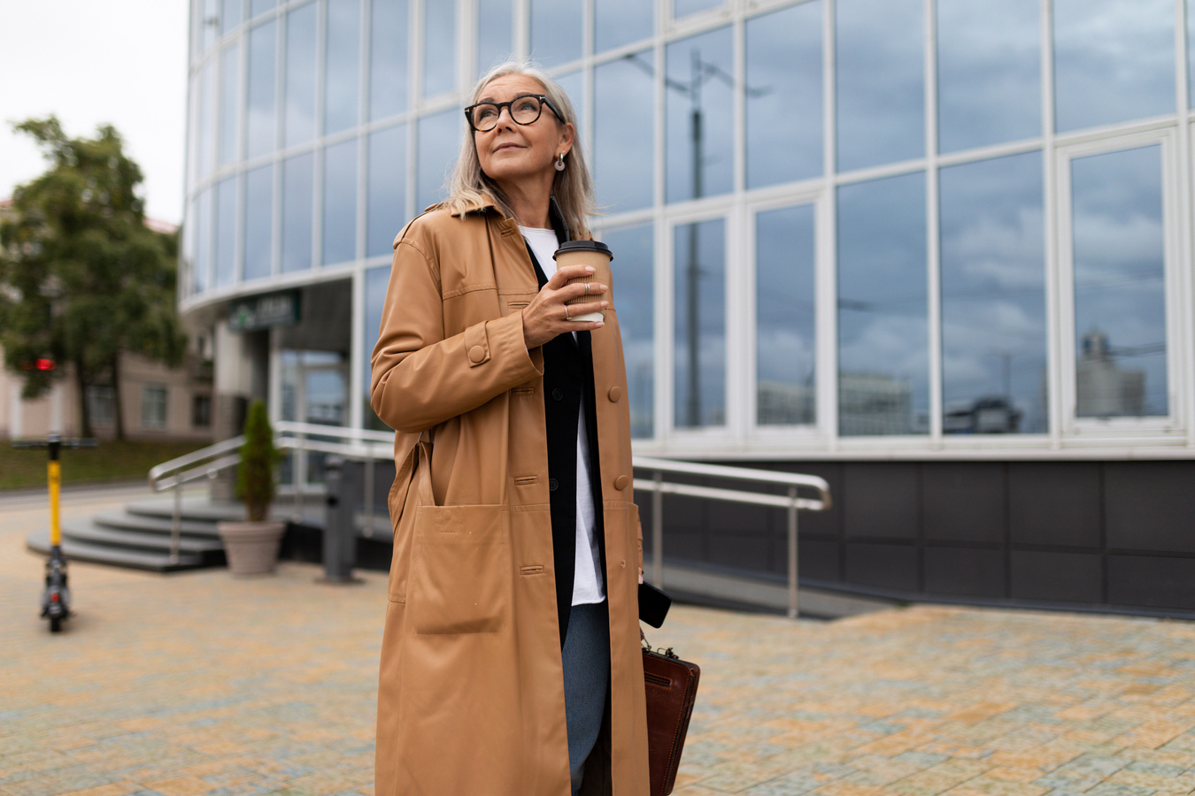Business Stylish Woman Head 50 Years Old Stands with a Glass of Coffee against the Backdrop of the Office Center